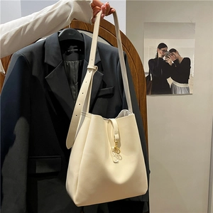 Minimalist beige leather bucket bag with gold hardware shown in a stylish studio setting