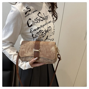 Close-up of brown suede handbag featuring a premium leather strap and golden H-shaped clasp