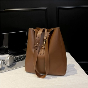 Minimalist brown leather bucket bag with gold hardware shown in an office setting