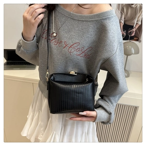 Detail of black pleated crossbody bag with gold snap closure on casual outfit
