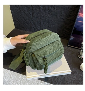 Detail of green corduroy crossbody bag with woven zipper pull and multi-pocket design