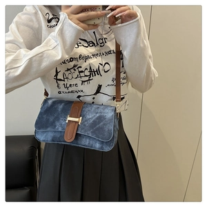 Detail of blue denim shoulder bag with leather strap and gold H-shaped buckle worn by model