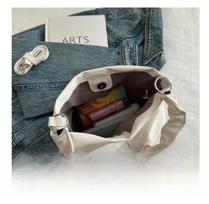 Detail of white pleated handbag showing bear logo tag and spacious interior storage