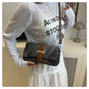 Detail of dark grey suede shoulder bag featuring a prominent gold H-shaped metal clasp