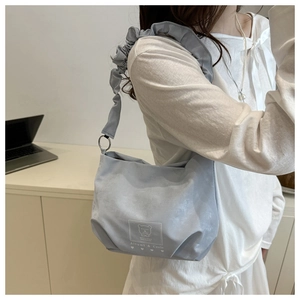 Detail of light blue shoulder bag featuring ruffled strap design and cute bear print logo