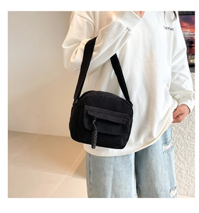 Close-up detail of black corduroy shoulder bag showing vertical texture and pocket