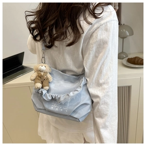 Detail of light blue canvas crossbody bag with ruffle edges and cute bear plush charm