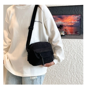 Detail of black corduroy crossbody bag featuring a woven zipper pull and soft texture