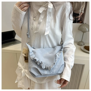 Detail of light blue crossbody bag featuring decorative ruffles and a plush bear pendant