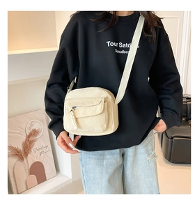 Detail of beige corduroy crossbody bag featuring a front zipper pocket and adjustable strap
