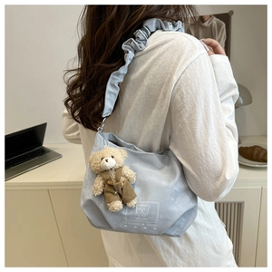 Detail of light blue pleated strap tote bag with cute bear plush charm decoration