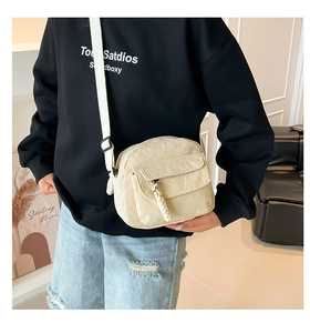 Detail of off-white corduroy crossbody bag showing soft ribbed texture and woven zipper pull