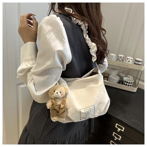 Detail of white tote bag with pleated strap and cute plush bear charm hanging on the side