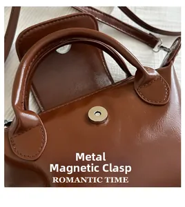 Close-up of brown PU leather handbag featuring a magnetic buckle and round handle detail