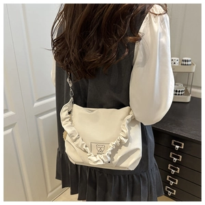 Detail of white crossbody bag featuring ruffled shoulder strap and cartoon bear patch