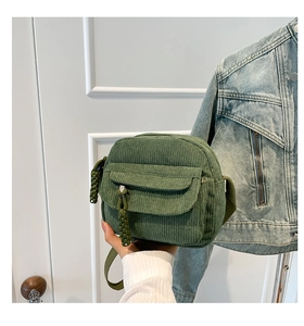 Detail view of a vintage forest green corduroy mini crossbody bag with woven zipper puller