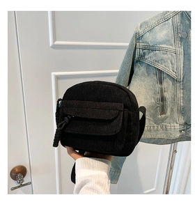 Detail of black corduroy mini crossbody bag featuring a front flap pocket and woven zipper pull