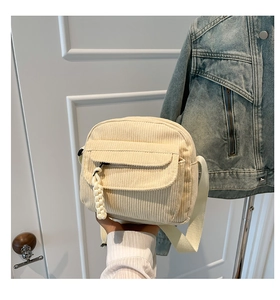 Detail of off-white corduroy crossbody bag featuring woven zipper and front pocket