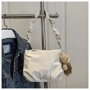 Close-up of white canvas shoulder bag with scrunchie strap and cute teddy bear charm