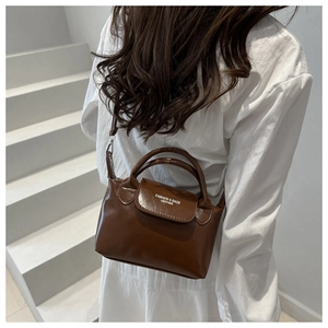 Brown mini crossbody bag in polished faux leather worn by a model in a white shirt