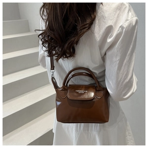 Rear view of model wearing a deep brown leather dumpling bag with contrast logo detail
