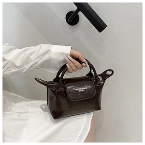 Close-up of deep brown glossy leather bag with rolled handles and fashion text detail