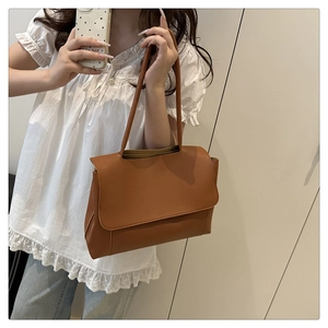 Close-up of brown faux leather tote bag being carried by a model against a white background