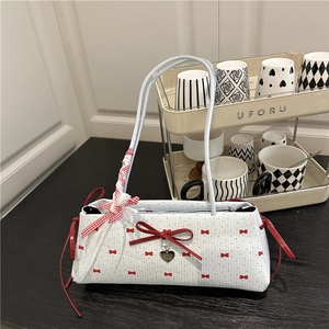 Sac à bandoulière blanc avec nœuds rouges et pendentif cœur sur table en bois noir