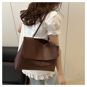 Detail view of large brown shoulder tote bag with flap closure worn with casual outfit
