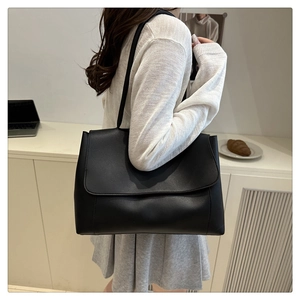 Minimalist large black leather tote bag shown on shoulder in a modern office setting