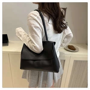 Rear view of a minimalist black faux leather tote bag worn on a woman shoulder