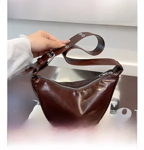 Close-up of brown crescent bag showing glossy PU leather and silver metal hardware details