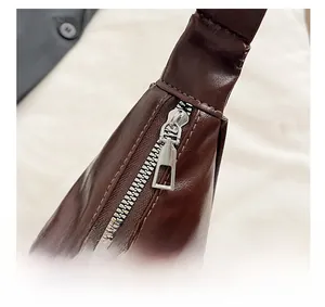 Detail of silver metal zipper and fine stitching on dark brown glossy leather bag