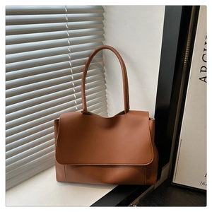 Detailed close-up of brown leather tote bag with flap closure and slim shoulder straps