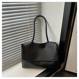 Detail of a black matte leather tote bag with long handles placed on a white windowsill