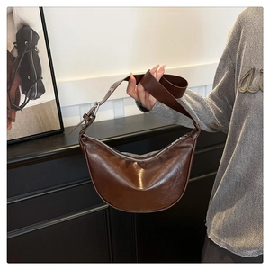 Close-up of brown crescent saddle bag with silver zipper and adjustable wide strap