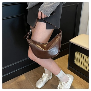 Brown half-moon saddle bag in glossy leather worn over the shoulder by a model