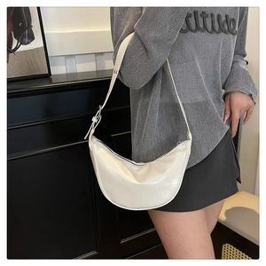 Detail of minimalist cream crescent bag with silver buckle and adjustable strap