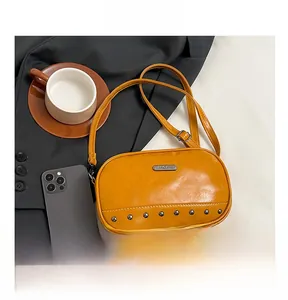 Detail of mustard yellow crossbody bag featuring bottom rivets and leather texture