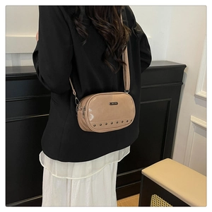 Detail view of khaki oval crossbody bag with metal rivets and fine leather strap