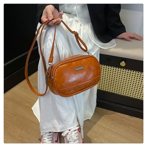 Detail of glossy leather crossbody bag featuring silver rivet trim and dual zippers