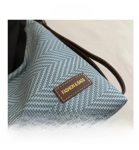 Detail shot of the blue and white woven texture with a brown leather logo patch on the bag
