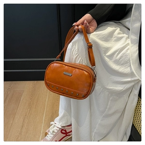 Detailed close-up of orange leather crossbody bag with metallic rivets and adjustable strap