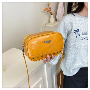 Detail of ginger yellow leather crossbody bag with silver rivet studs and metal logo plate