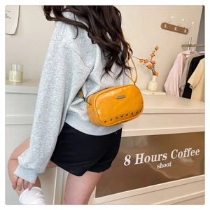 Close-up of yellow vintage camera bag with metal studs worn by a model in a cafe