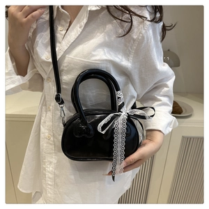Detail of black glossy shell bag featuring relief bow texture and white lace ribbon bow