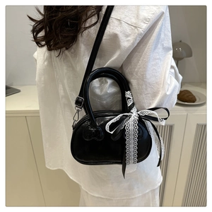 Close-up of black matte handbag featuring an embossed heart and lace bow detail