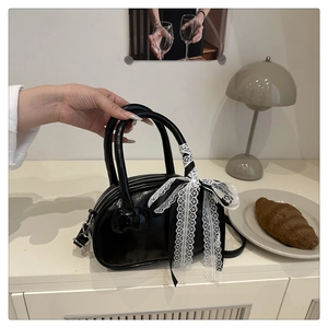 Detail of a black glossy handbag with elegant white lace bow decoration and rounded handles