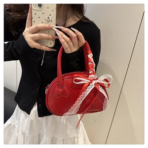 Detail view of red glossy handbag with white lace bow and heart patch held by model