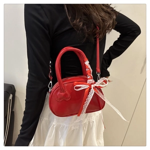 Detail of red crossbody bag featuring heart decor and white lace bow on the handle